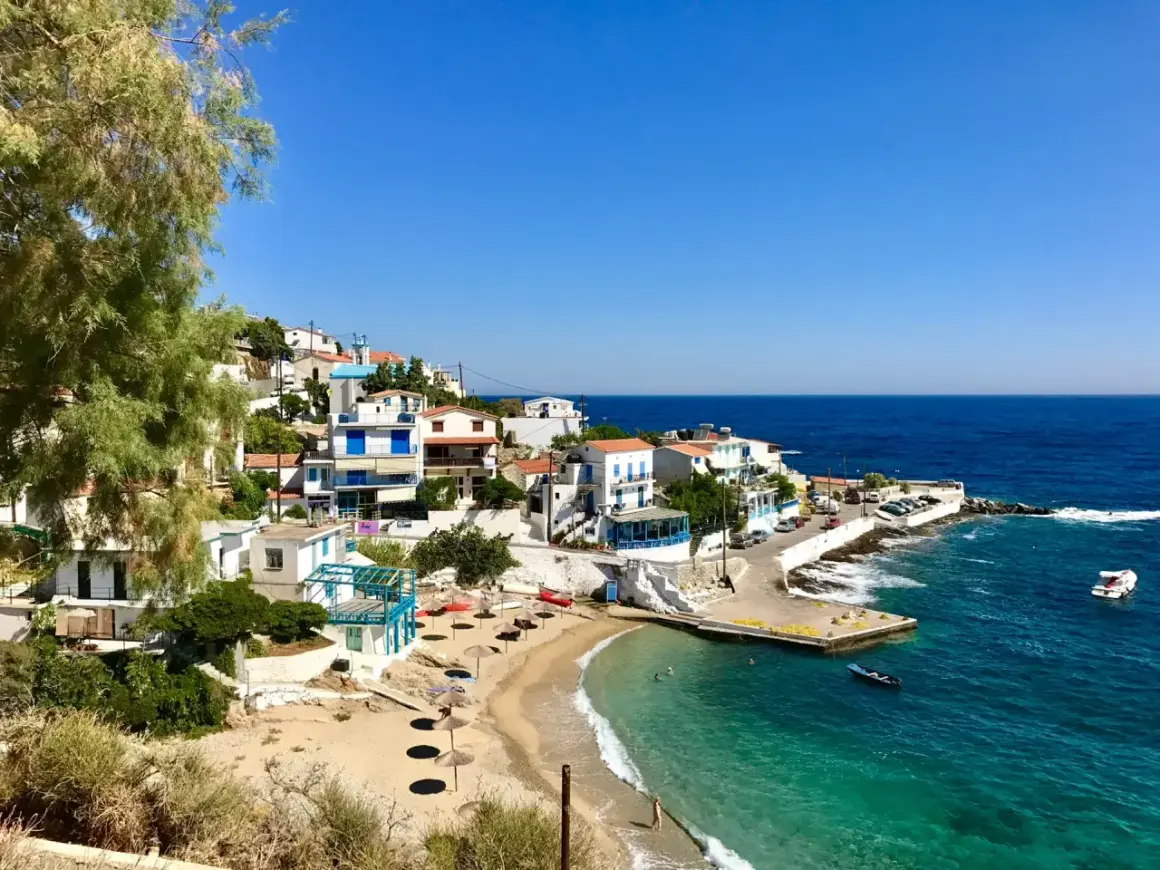 En pittoresk kustby på Ikaria, Grekland, med vita hus, en sandstrand och turkost vatten.