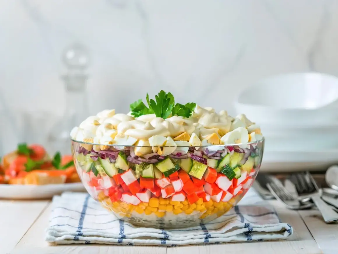 Deliciosa ensalada de surimi en capas, con maíz, pepino, cebolla morada y huevo duro, cubierta de mayonesa y perejil.
