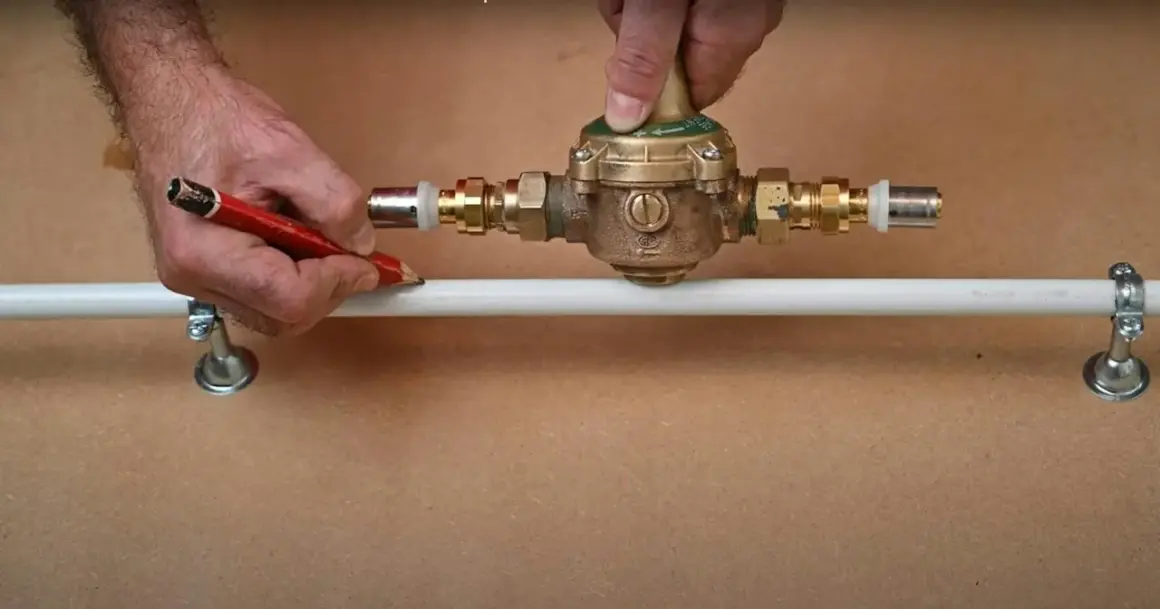 Ajustement d'un réducteur de pression pour comment augmenter la pression d'eau. Un homme marque un tuyau avec un crayon.