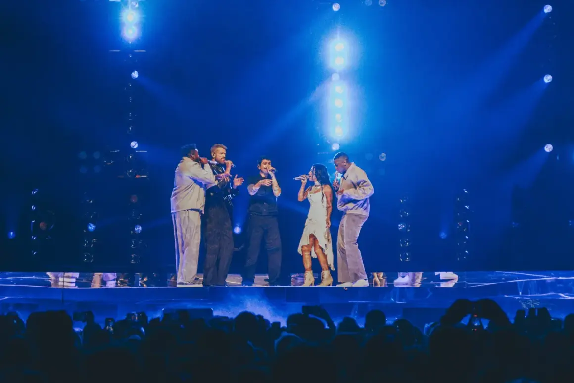 Zespół Pentatonix występuje na scenie w blasku niebieskich świateł, śpiewając do mikrofonów.