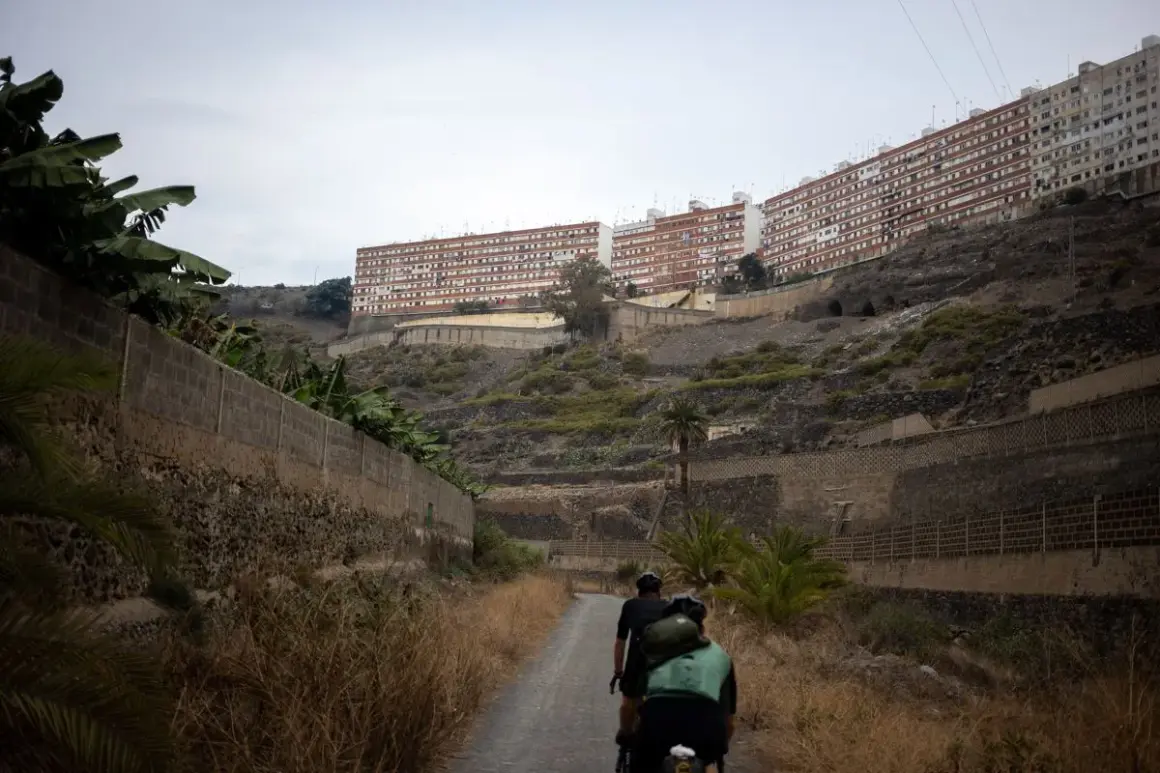 Ciclistas recorren el **barranco de Guiniguada**, con edificios residenciales en la ladera y vegetación seca.