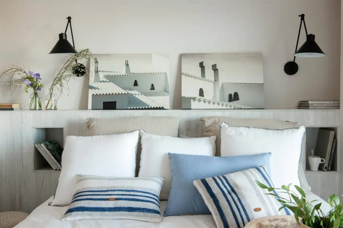 Ideas para hacer un cabecero: dos cuadros de tejados blancos, lámparas negras y cojines a rayas sobre una cama.