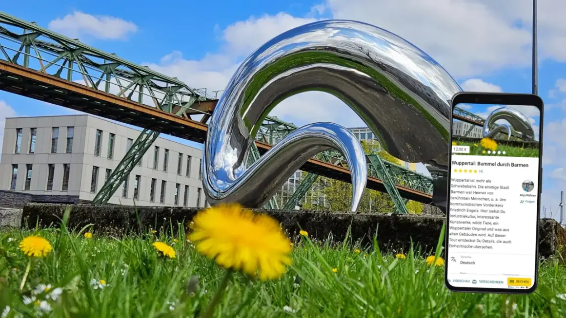 Moderne Skulptur vor Schwebebahn und Gebäude in Wuppertal. Ein Handy zeigt eine Tour durch Barmen, ein tolles Ziel für Ausflugsziele Wuppertal.