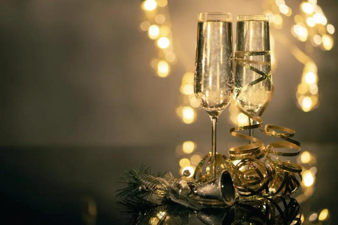 Deux flûtes de champagne pétillant, décorées de rubans dorés, prêtes pour organiser une soirée de nouvel an. Lumières festives en arrière-plan.