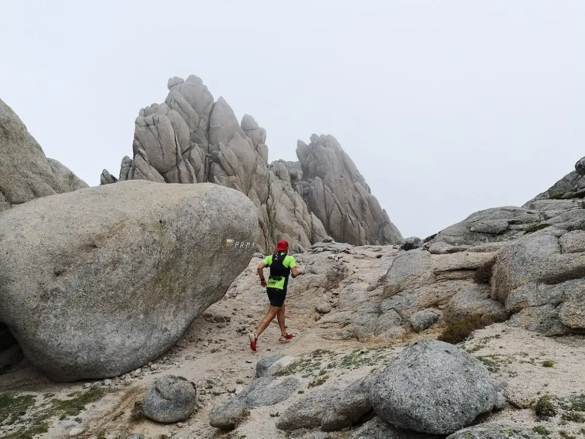 Un coureur en tenue de trail suit le sentier balisé PR-M1, traversant un paysage rocheux et brumeux.