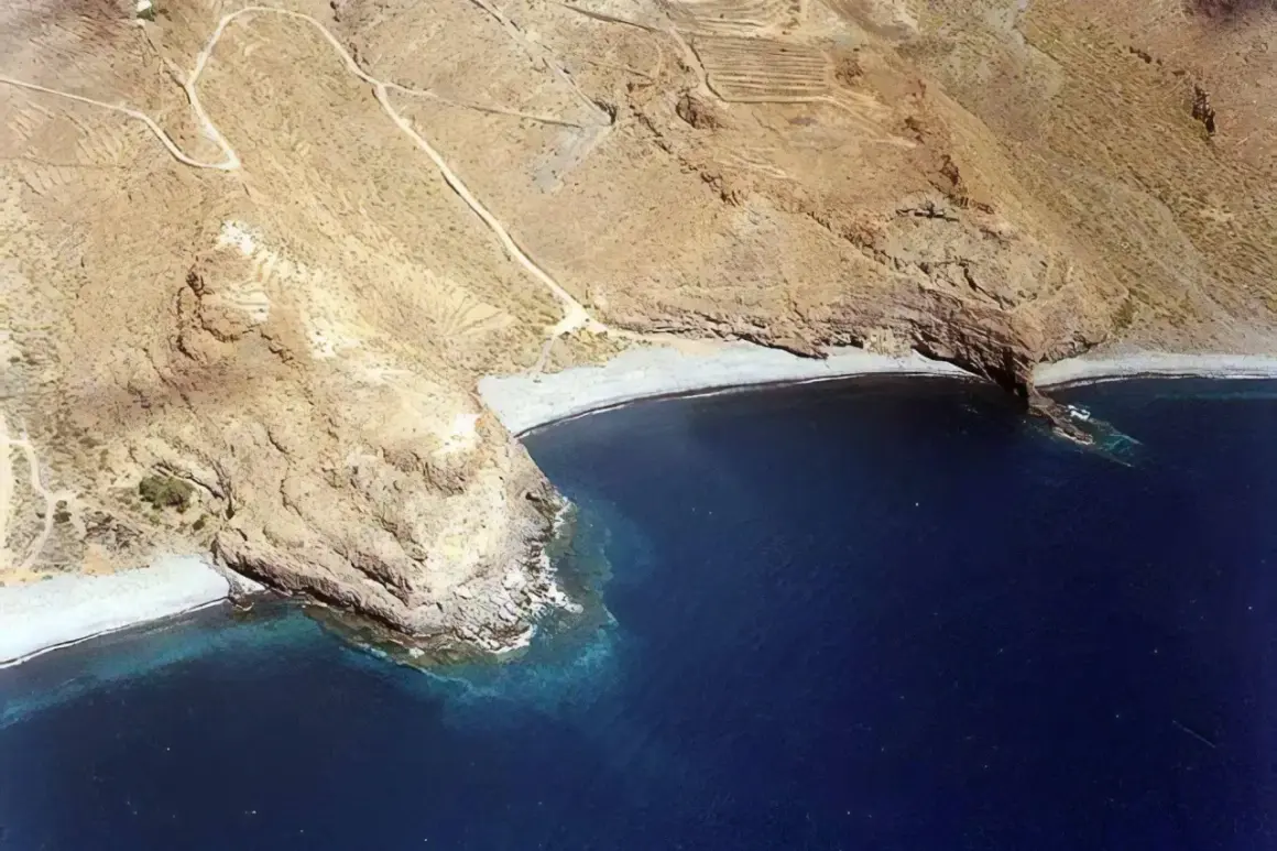 Vista aérea de la playa del medio, una cala rocosa con aguas azules profundas y senderos en las laderas áridas.