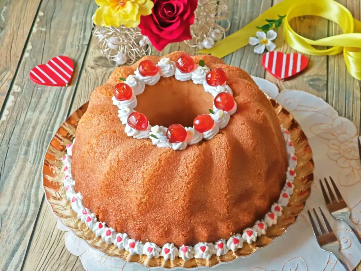 Delicioso bizcocho con forma de anillo, decorado con crema, cerezas y corazones. Un dulce baba al ron perfecto para celebrar.