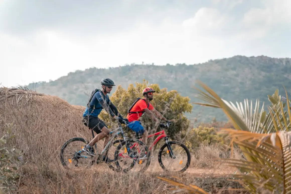 Dos ciclistas disfrutan de rutas en bici para principiantes en un paisaje rural con colinas y vegetación seca.