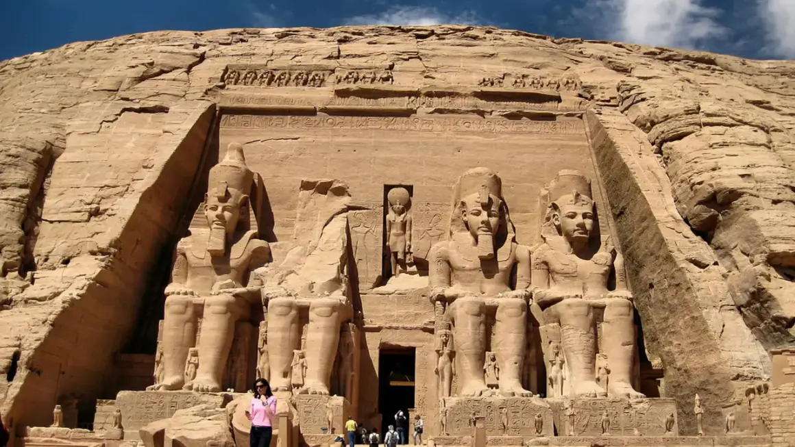 Gigantescas estatuas de Ramsés II flanquean la entrada del templo de Abu Simbel, Egipto. Un pequeño grupo de turistas admira la magnificencia de esta maravilla antigua.