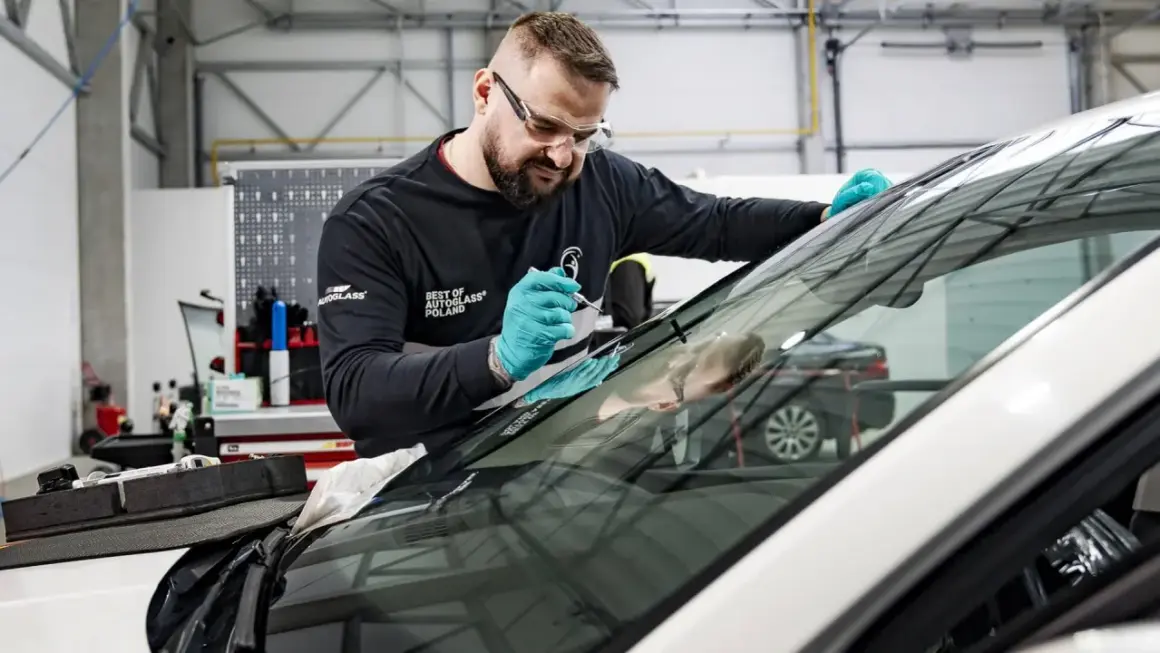 Mechanik w okularach ochronnych i rękawiczkach naprawia szybę samochodową.
