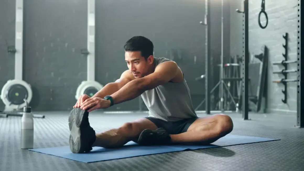 Mann dehnt sich im Fitnessstudio, um den Muskelaufbau zu unterstützen.