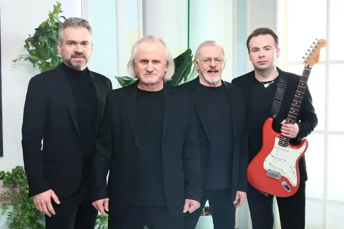 Czterech mężczyzn w czarnych strojach. Jeden z nich trzyma czerwoną gitarę.