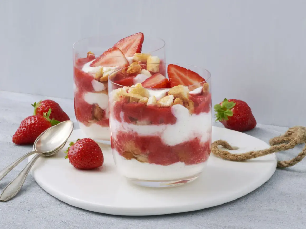 Zwei Gläser mit einem sommerlichen Dessert aus Erdbeeren und Sahne, garniert mit frischen Erdbeerscheiben und Keksstückchen. Ein schnell und einfach zubereitetes Genusserlebnis.