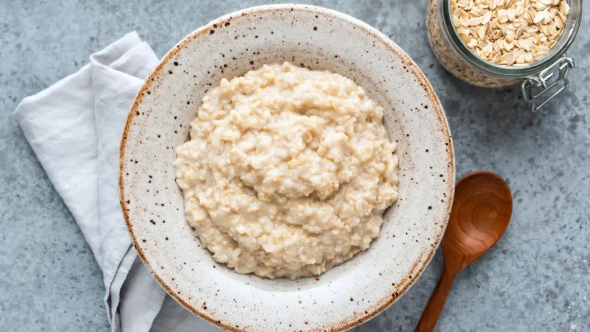 Cremiger Porridge im rustikalen Teller, daneben Haferflocken im Glas. Ein einfaches Porridge Rezept für einen guten Start.
