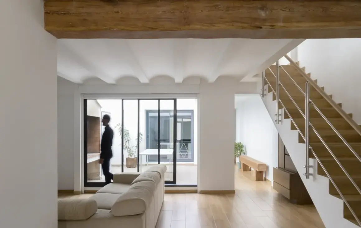 Interior moderno con vigas de madera, escaleras y un hombre mirando al patio. Estimación del precio construir casa 30 m2.