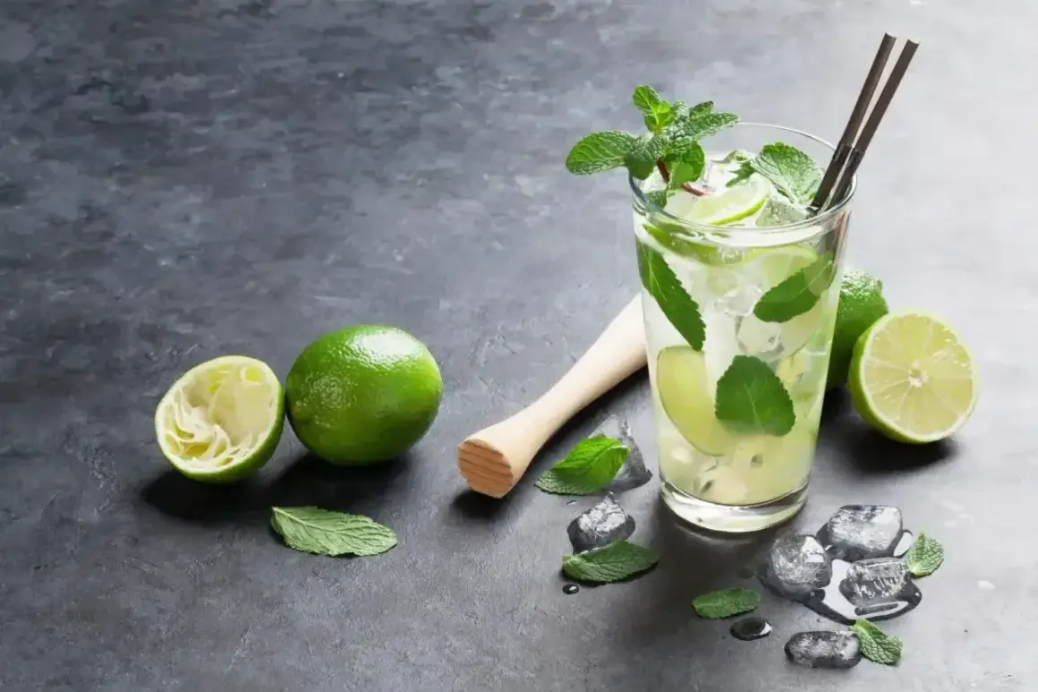 Orzeźwiający mohito smak: szklanka z lodem, limonkami i miętą, obok wyciśnięta limonka i tłuczek.