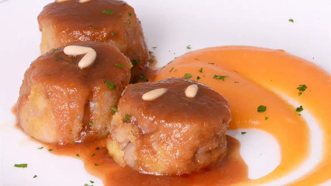 Deliciosas manitas de cerdo rellenas, bañadas en salsa y decoradas con piñones y perejil, acompañadas de puré de zanahoria.