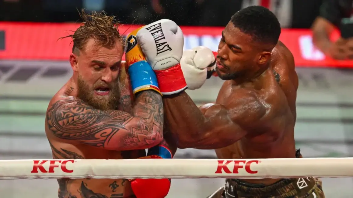 Two boxers grapple in the ring. One, with tattoos and wet hair, recoils from a punch. The other, muscular and focused, lands a blow. This is what heavyweight boxing looks like.