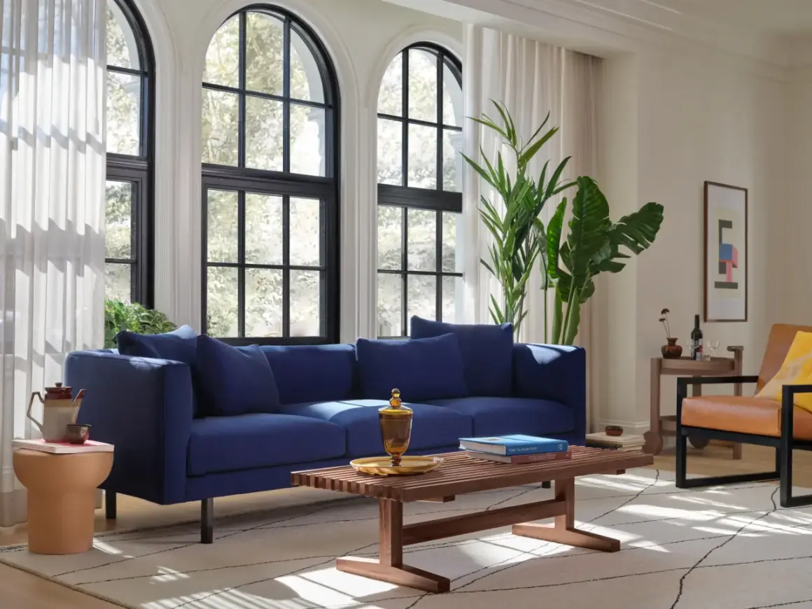 Granatowy salon inspiracje: nowoczesna sofa, drewniana ława, skórzany fotel i duże okna tworzą przytulną przestrzeń.