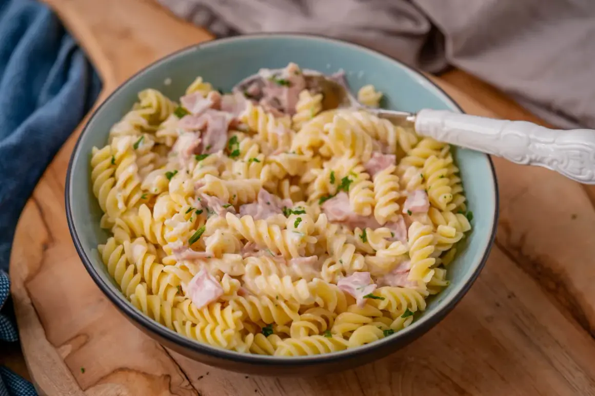Fusilli-Nudeln in cremiger Schinken-Sahne-Sauce, garniert mit Petersilie. Ein köstliches Gericht, das zum Genießen einlädt.