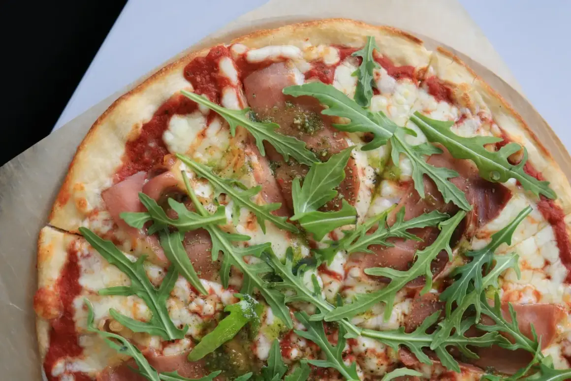 Pyszna pizza prosciutto z rukolą i sosem pesto.