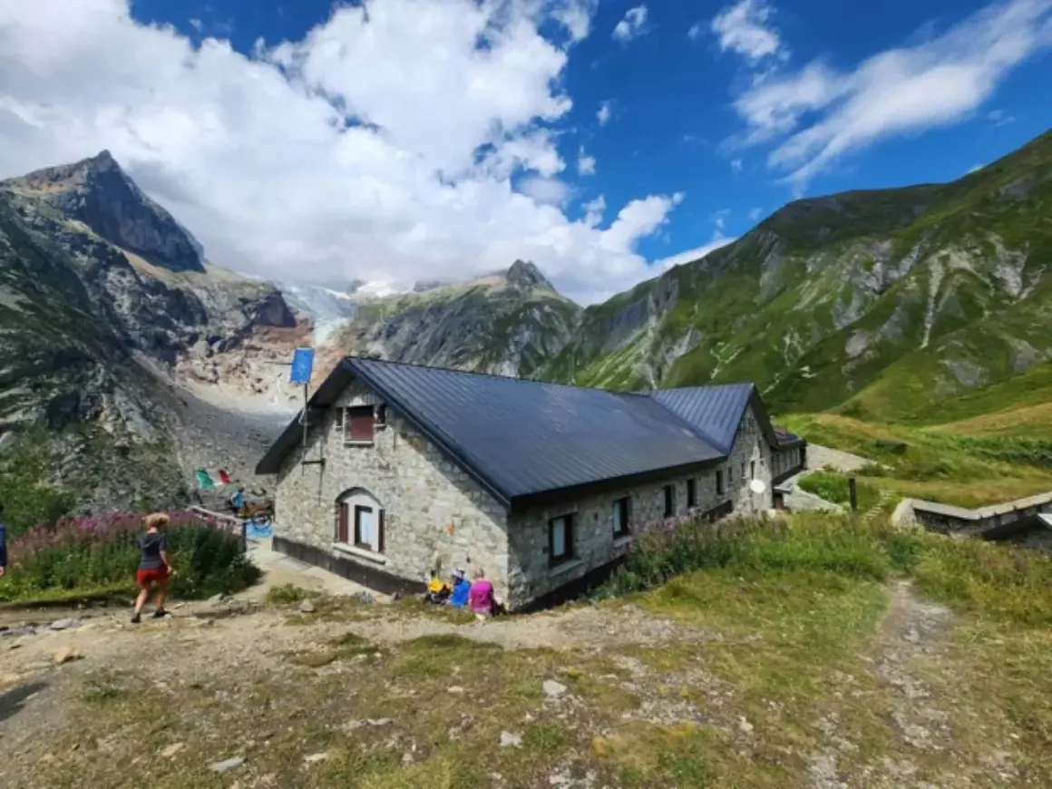 Kamienny schron na GR20 Korsyka, z lodowcem w tle i zielonymi górami.