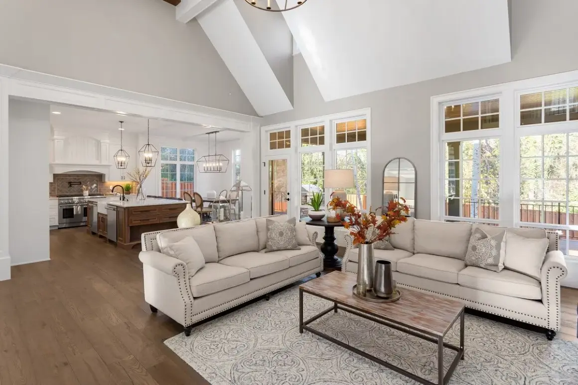 Stilvolles wohnzimmer einrichten mit beigen Sofas, Holzboden und offener Küche. Ein moderner Teppich und ein Couchtisch runden das Bild ab.