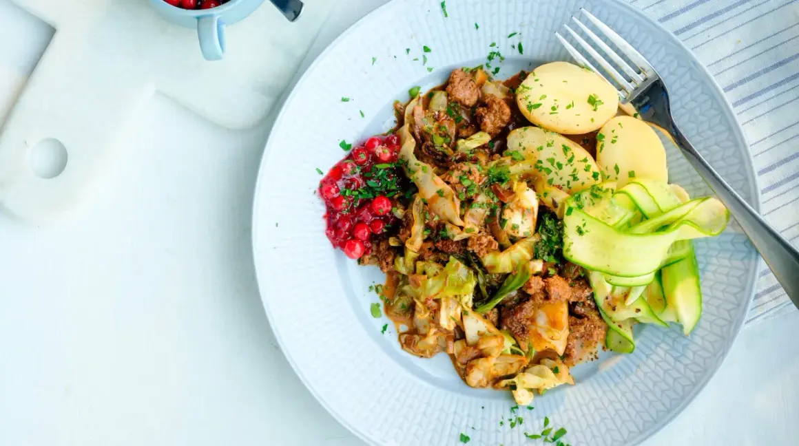 En tallrik med stuvad vitkål, köttfärs, kokt potatis, gurkband och rårörda lingon. Ett härligt kålmaja recept för en smakrik middag.