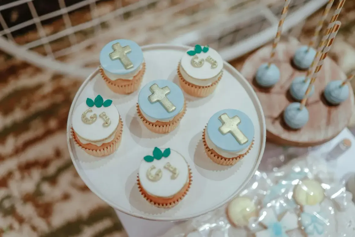 Jolis cupcakes décorés de croix dorées et de lettres pour un menu baptême à faire soi même. Des cake pops bleus sont aussi visibles.