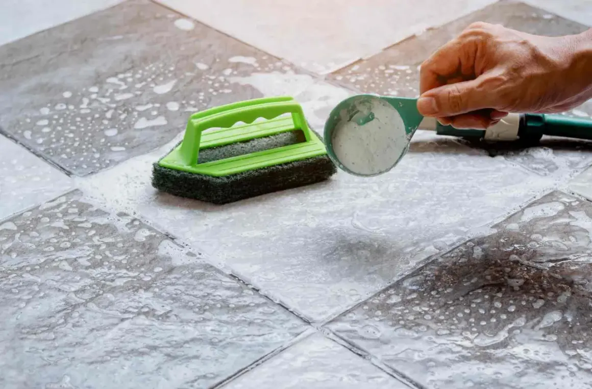 Nettoyer carrelage neuf qui laisse un voile blanc : une brosse verte et une cuillère de poudre sur le sol mouillé.