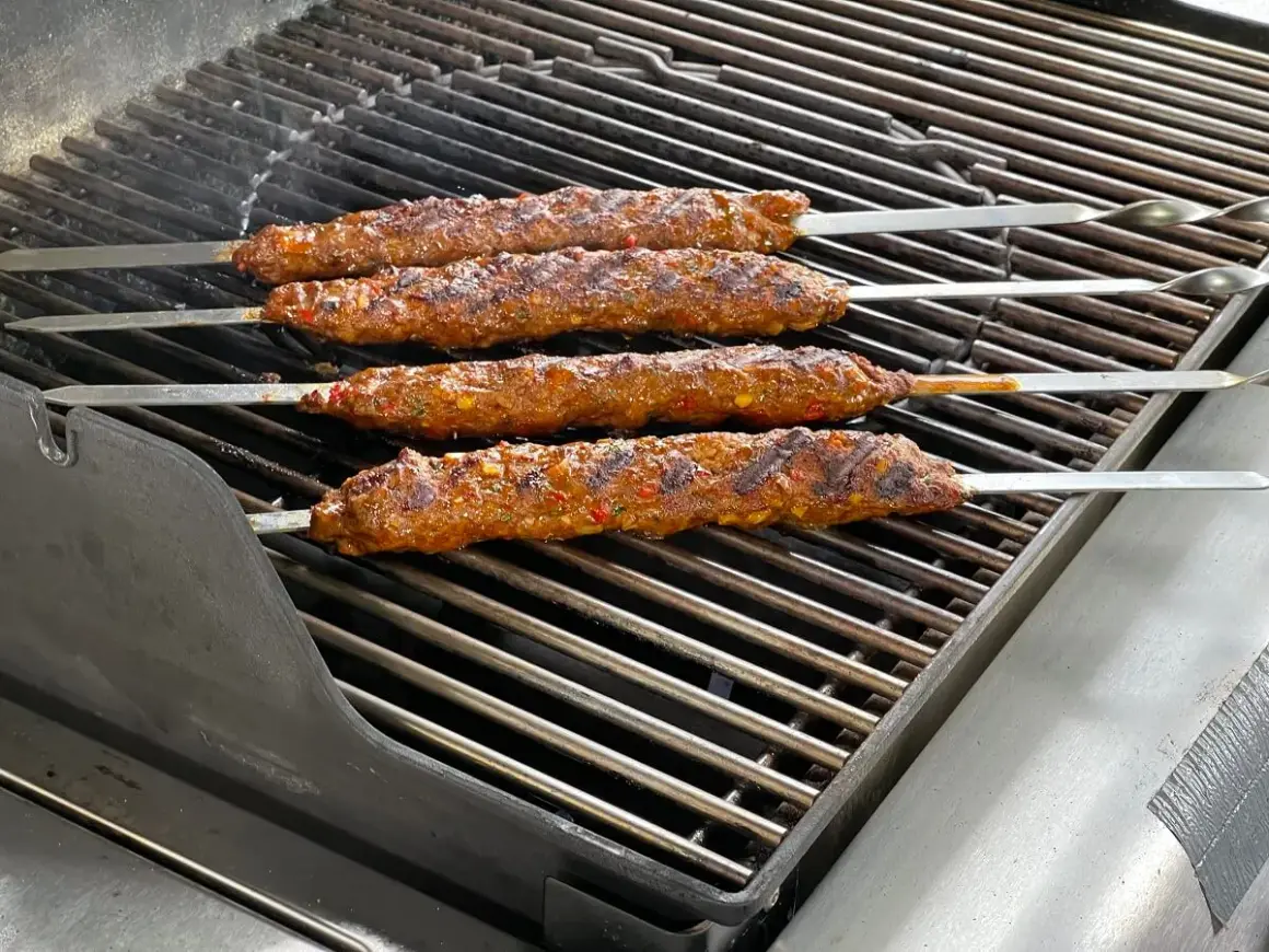 Vier saftige Adana Kebap Spieße brutzeln auf dem Grill. Das perfekte Adana Kebap Rezept für den Sommer.