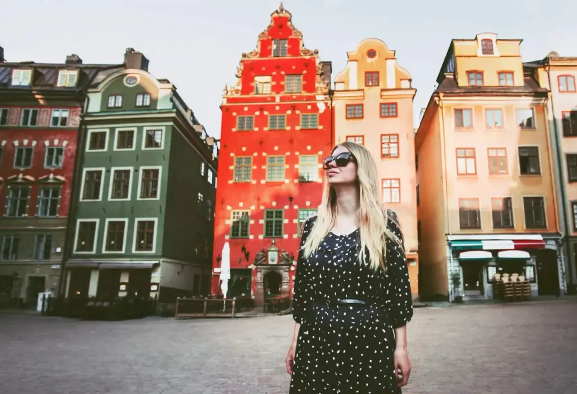 En kvinna med solglasögon står framför färgglada hus på ett torg. Kanske är detta sveriges vackraste stad.