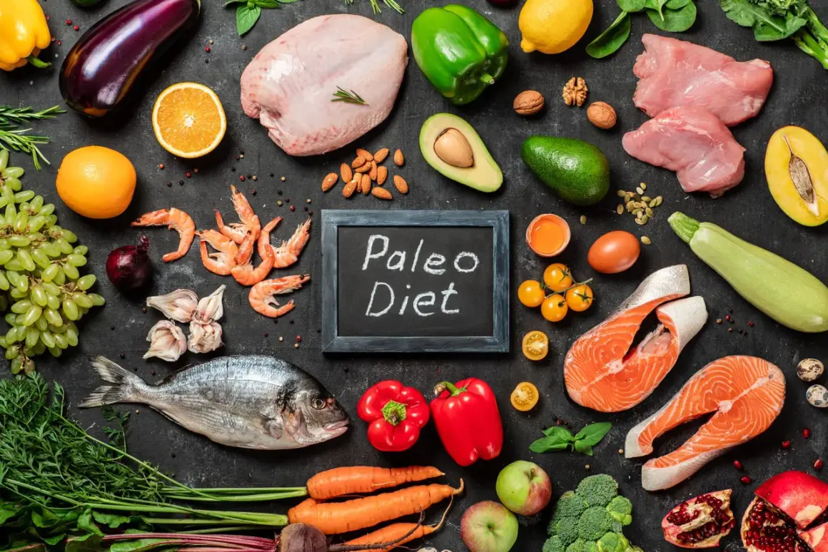 Na czarnej tablicy napis "Paleo Diet". Wokół świeże ryby, mięso, owoce, warzywa i orzechy – składniki diety paleo.