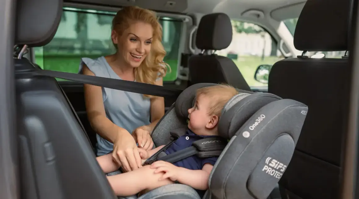Lächelnde Mutter sichert ihr Baby im Kindersitz vorne im Auto.