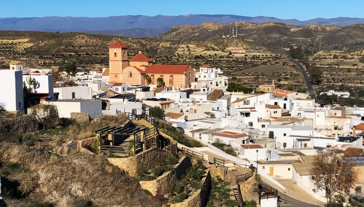 Vista panorámica de Lucainena de las Torres, un pueblo blanco andaluz con una iglesia de tejado naranja y montañas al fondo. ¡Un lugar con mucho que ver!