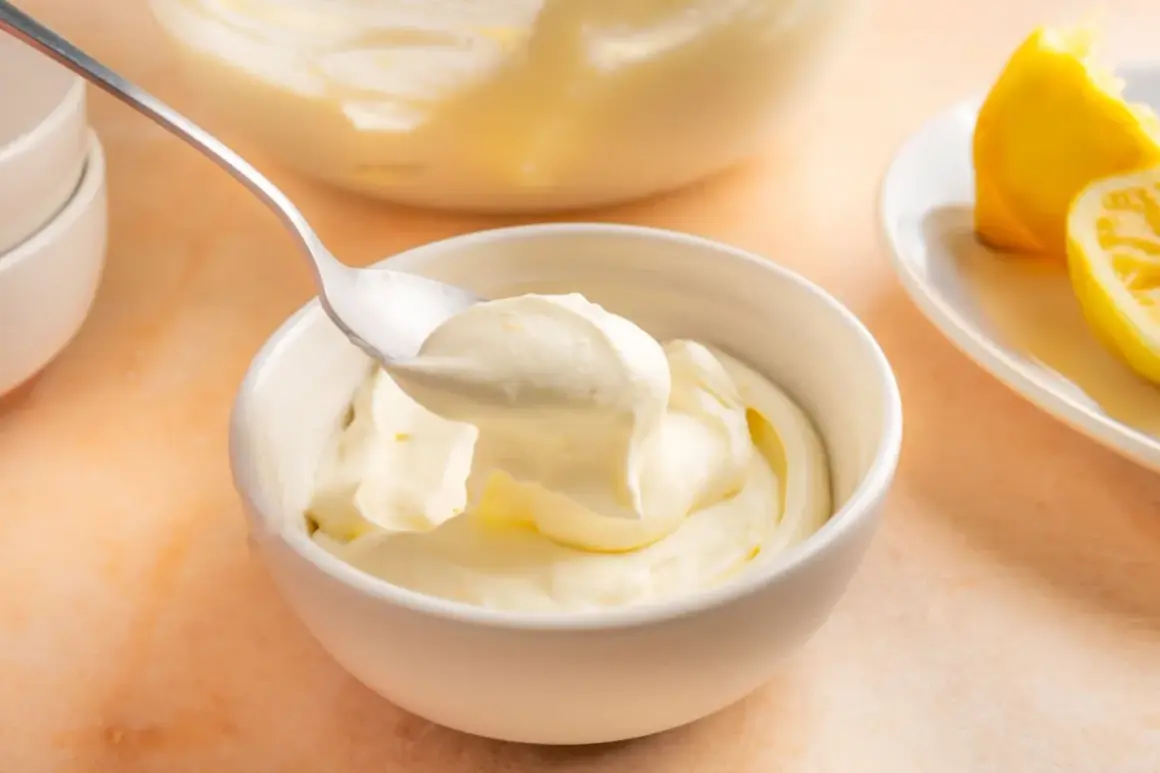 En sked lyfter krämig citronmousse ur en skål. Bredvid ligger citronklyftor, redo att förhöja smaken av citronmousse med lemoncurd.