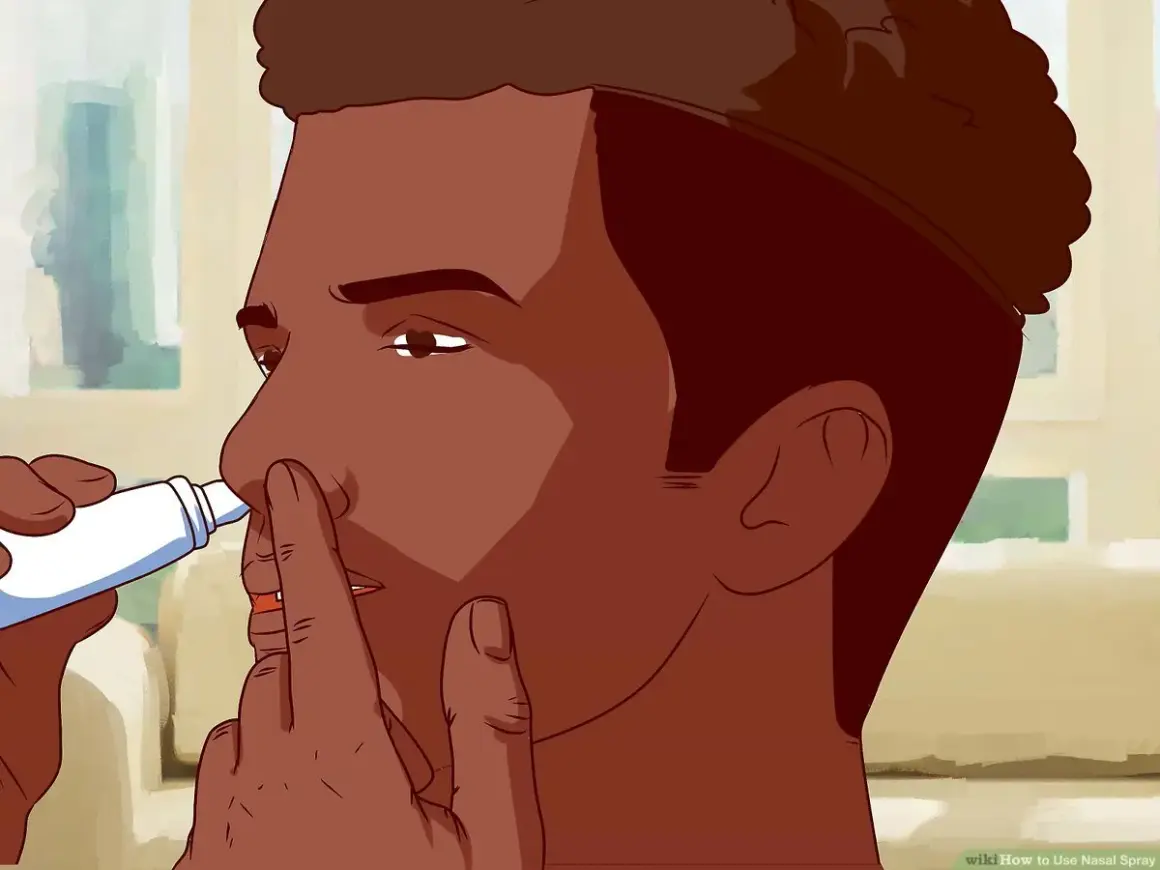 Mężczyzna aplikuje spray do nosa, przykładając końcówkę do jednej z dziurek.