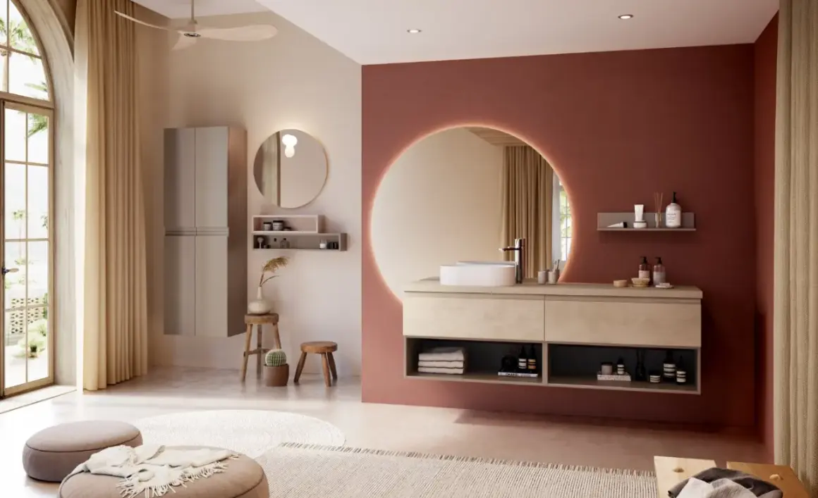 Salle de bain moderne avec murs rose terre et beige, meuble vasque en bois clair, miroir rond lumineux. La couleur salle de bain est chaleureuse et apaisante.