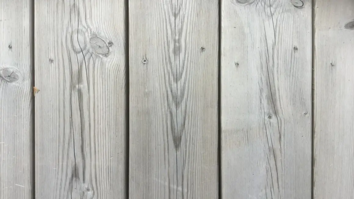 Grå träplankor med synliga kvistar och ådring, som en kisel altan i sommarsolen.
