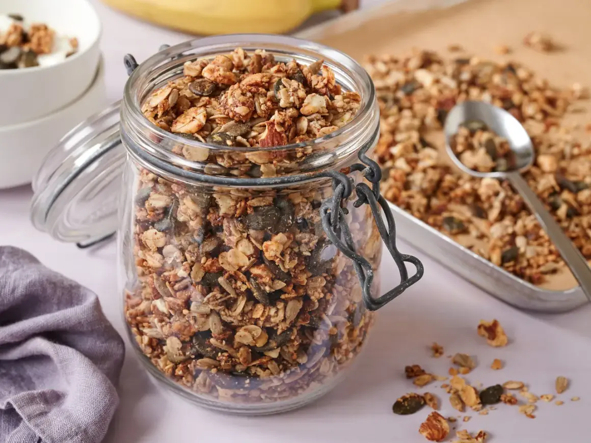Ein Glas voller knusprigem, selbstgemachtem Granola ohne Zucker, mit Nüssen und Kernen. Perfekt für ein gesundes Frühstück.