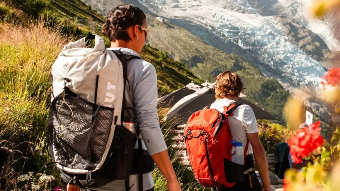 Zwei Wanderer mit Rucksäcken auf einem Bergpfad. Die Frage "was zieht man zum wandern an" wird durch ihre funktionale Kleidung beantwortet.