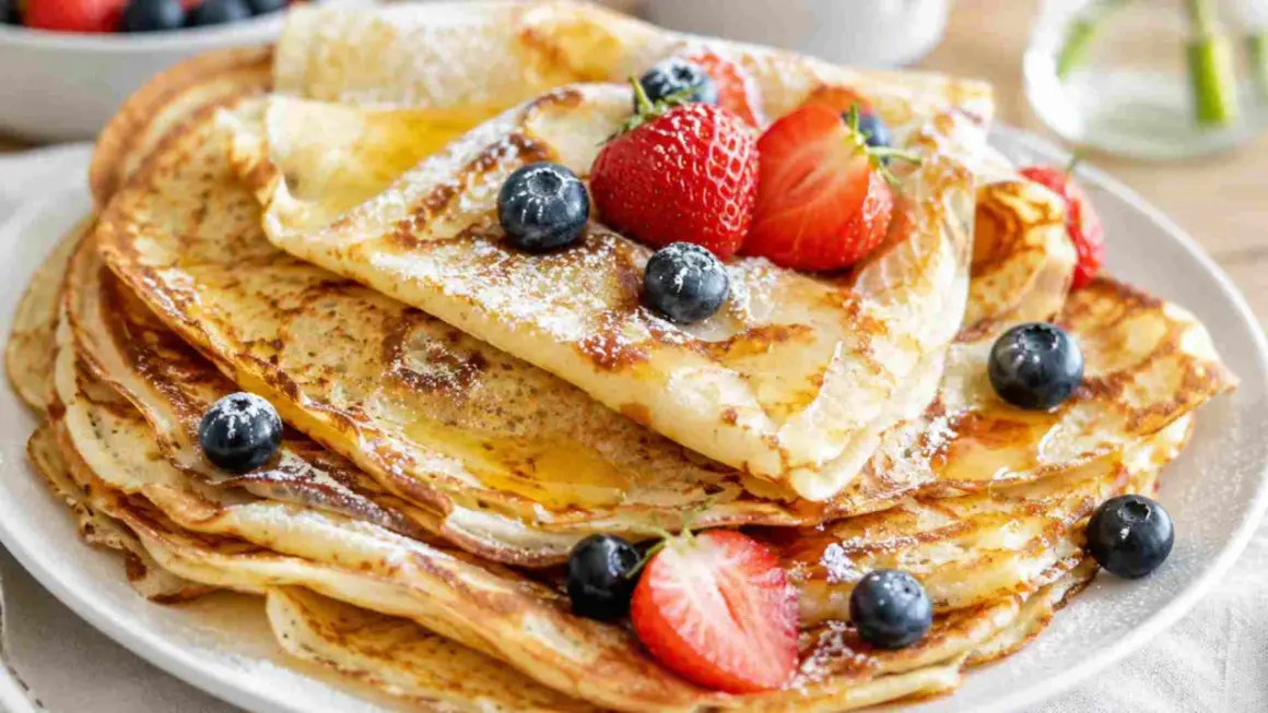 Ein Stapel goldbrauner Pfannkuchen, bestäubt mit Puderzucker und garniert mit frischen Beeren und Honig. Ein einfaches Pfannkuchen-Rezept, das jeden Tag zum Genuss macht.