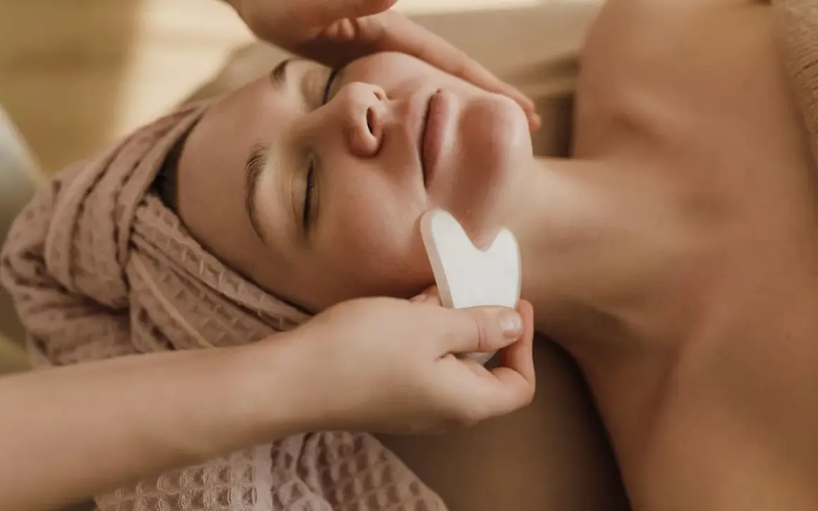 Un viso rilassato riceve un massaggio con pietra gua sha, una tecnica che serve a migliorare la circolazione e il drenaggio linfatico, donando luminosità.