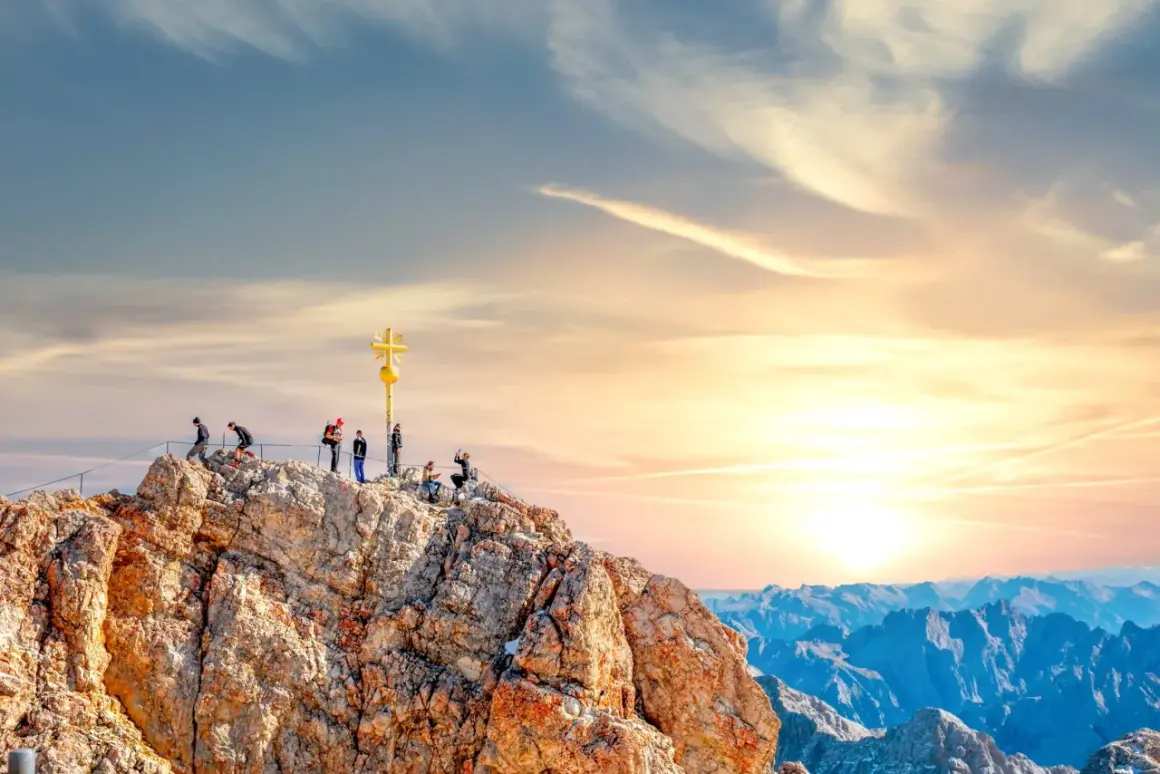 Menschen auf dem Gipfel der Zugspitze mit goldenem Kreuz. Die Zugspitze Aufstieg Dauer ist lang, aber die Aussicht ist es wert.