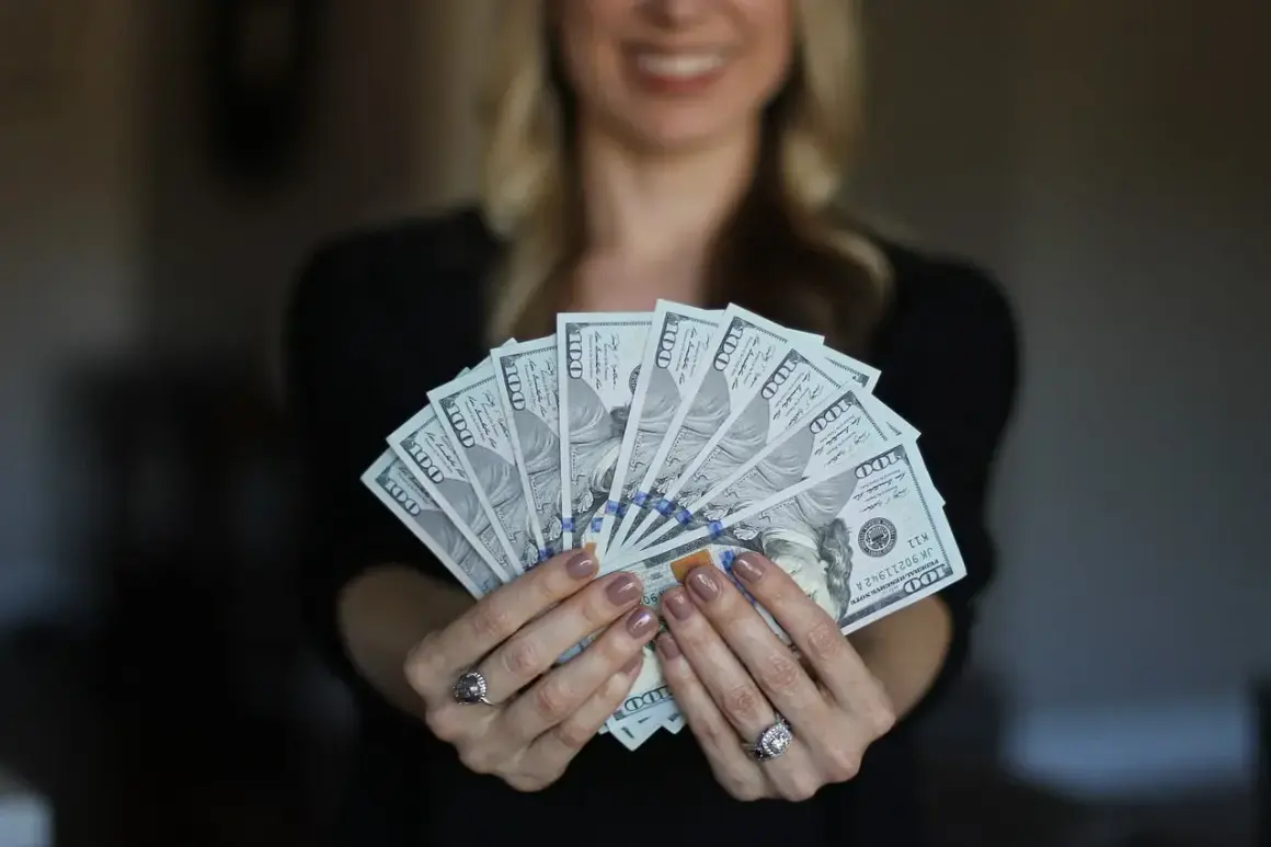 Uśmiechnięta kobieta trzyma wachlarz banknotów 100-dolarowych. Czy Vivus wyplaca w sobotę?