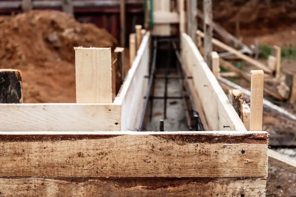 Drewniana szalunkowa konstrukcja przygotowana pod fundament pod ogrodzenie. W środku widoczna zbrojenie.
