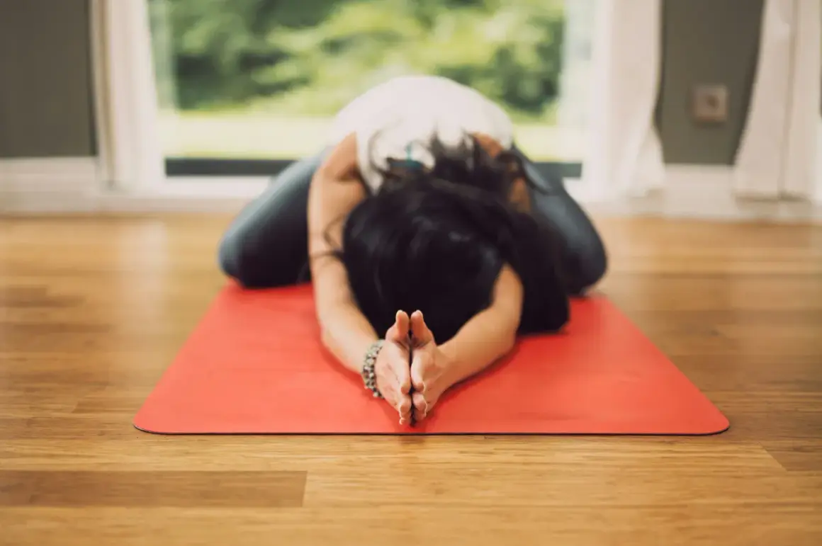 Mujer en postura de niño en esterilla roja, practicando una de las 20 posturas de yin yoga.