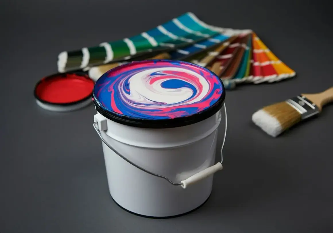 Farbeimer mit verwirbelten Farben, daneben ein Pinsel und Farbfächer. Ideal für eine Tabelle zum Farben selber mischen.