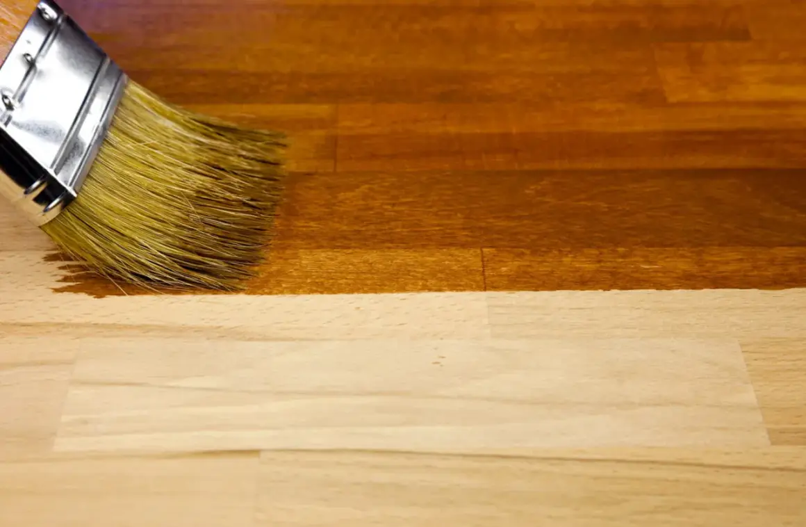 Un pinceau applique un vernis pour foncer du bois, transformant le bois clair en une teinte chaude et profonde.