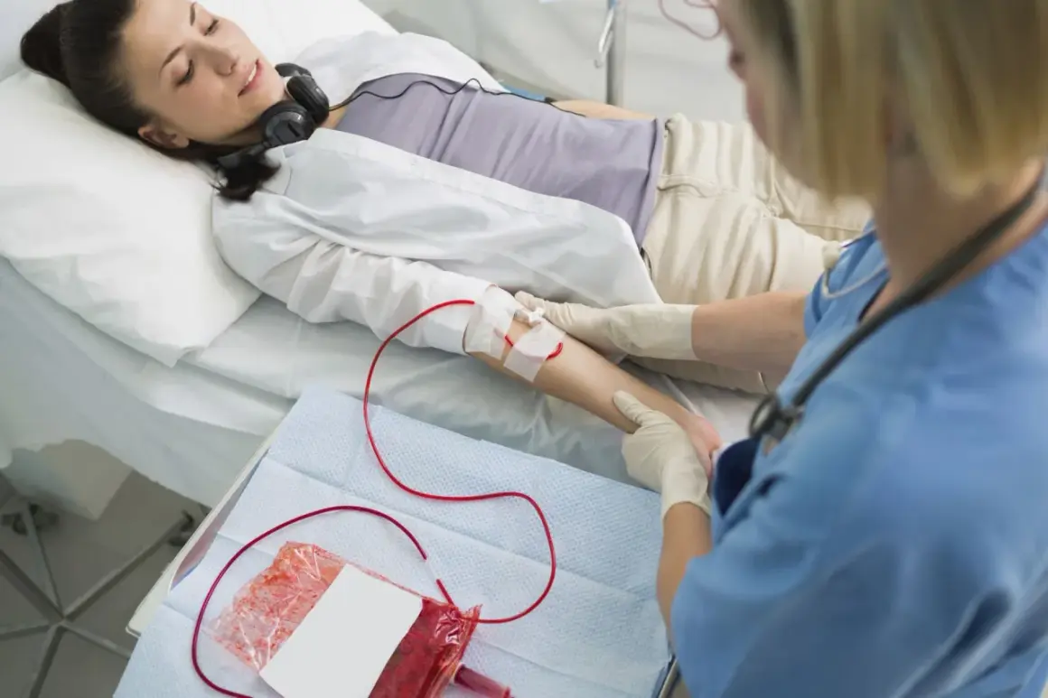 Kobieta leży w łóżku, słuchając muzyki przez słuchawki, podczas gdy pielęgniarka wykonuje przetaczanie krwi.